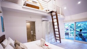 Ein Schlafzimmer mit Hochbett, einer Leiter, einem großen Fenster mit Blick auf Palmen und einem Badezimmer mit Tür und Handtuchhalter.