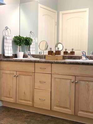 A bathroom with a granite countertop, wooden cabinets, a potted plant, a mirror, and a towel rack.