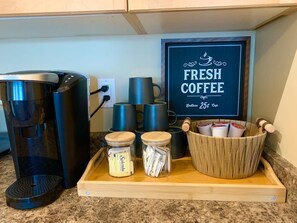 A coffee station with a coffee maker, cups, and a tray with jars and a wooden container.