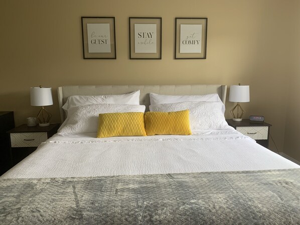 A hotel room with a bed, two bedside lamps, and three framed motivational quotes on the wall.