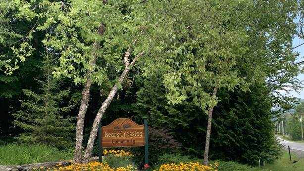 A sign for Bears Crossing Community surrounded by a garden with various flowers and trees.