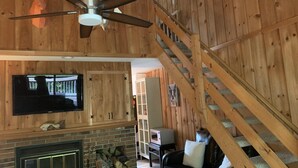 A wooden interior with a fireplace, a TV mounted on the wall, and a staircase.