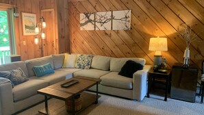 A cozy living room with a wooden wall, a beige sofa, a coffee table, and a lamp.