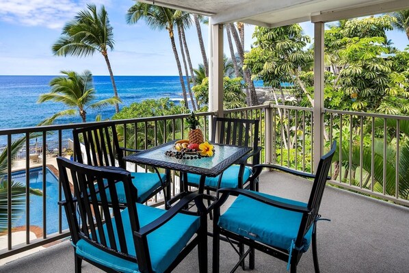 Un balcon avec une table et des chaises, donnant sur une piscine et l’océan.
