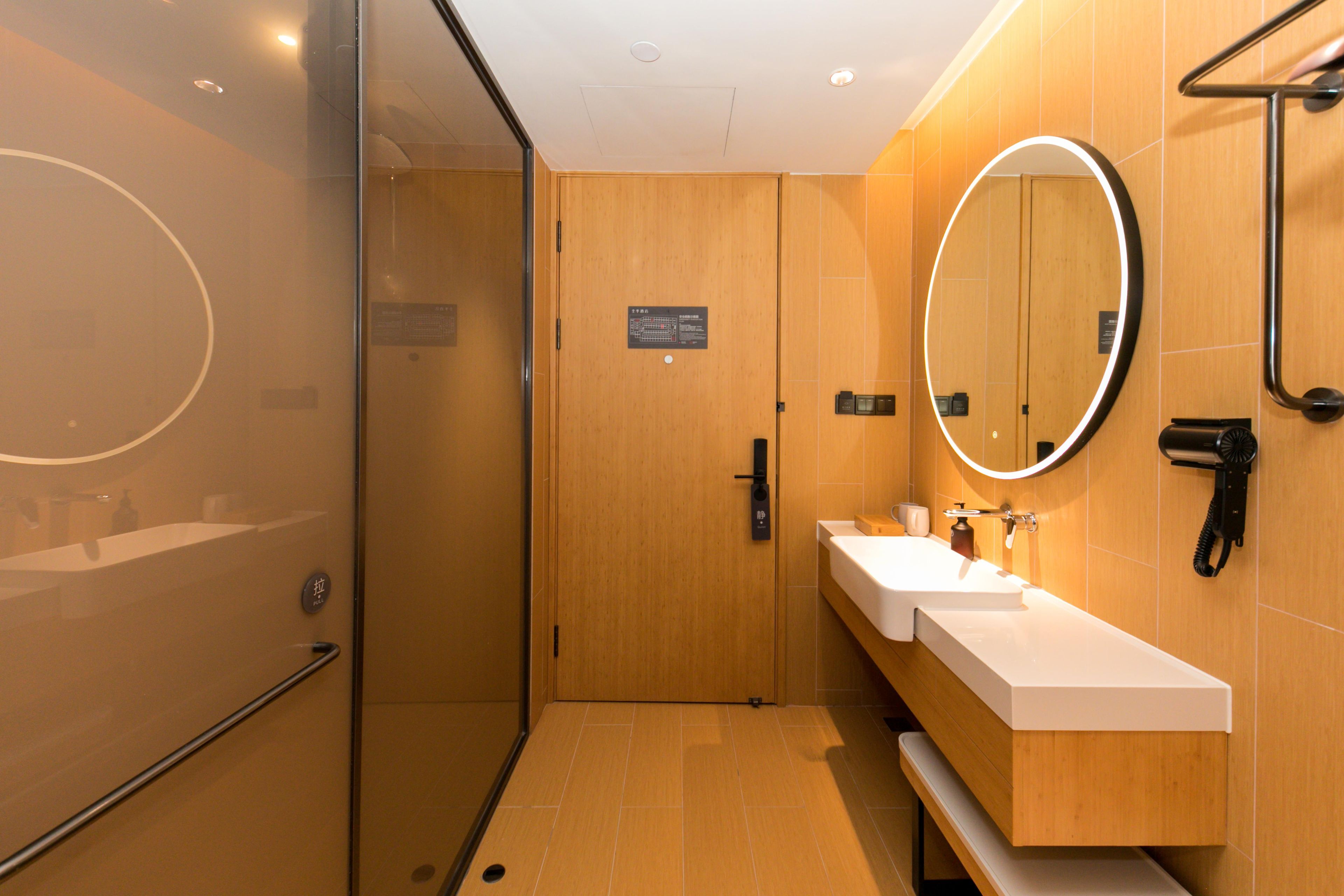 A modern bathroom with a glass shower enclosure, a wooden vanity with a white sink, and a round mirror.