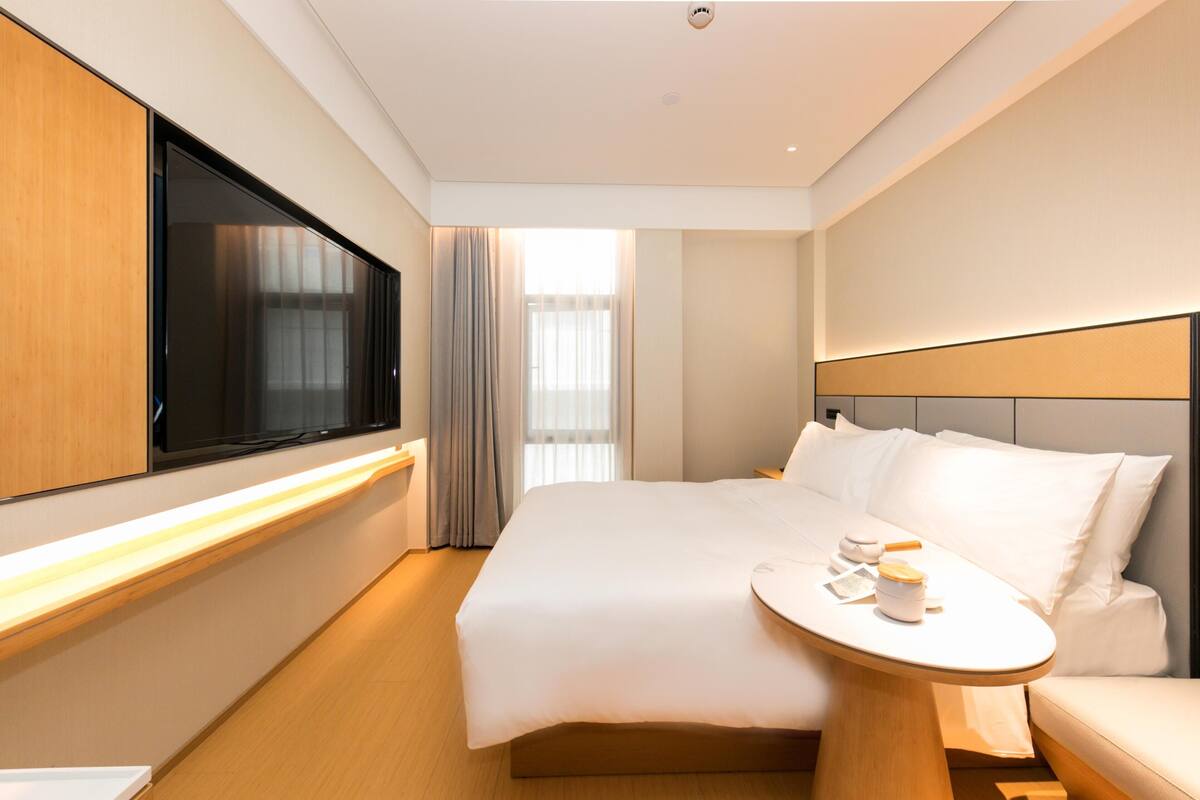A modern hotel room with a large bed, bedside table, and a flat-screen TV.
