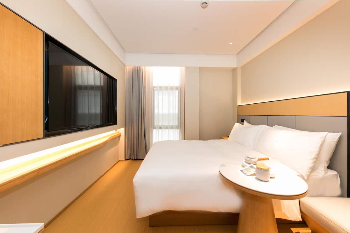A modern hotel room with a large bed, bedside table, and a flat-screen TV.