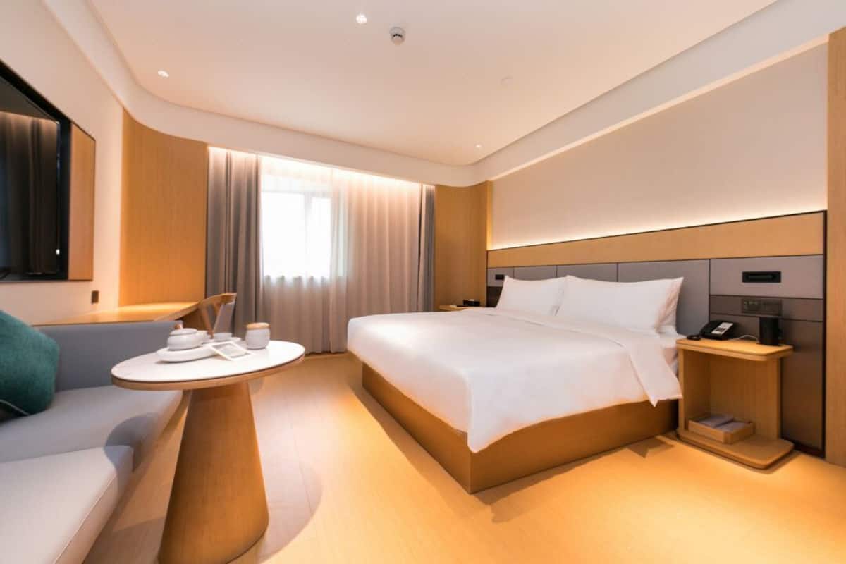A modern hotel room with a bed, bedside table, and a small seating area with a table.