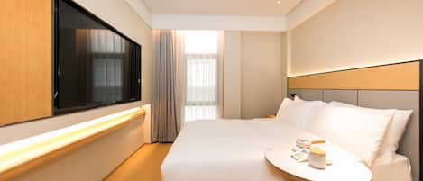 A modern hotel room with a large bed, bedside table, and a flat-screen TV.