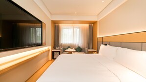 A hotel room with a large bed, a TV, a small table with a chair, and a window with curtains.