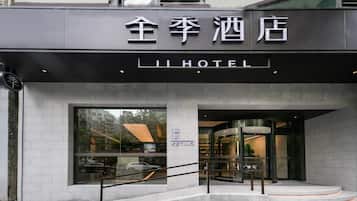 Entrada de hotel com design moderno, destacando uma placa com caracteres chineses e a palavra 'HOTEL' em inglês.