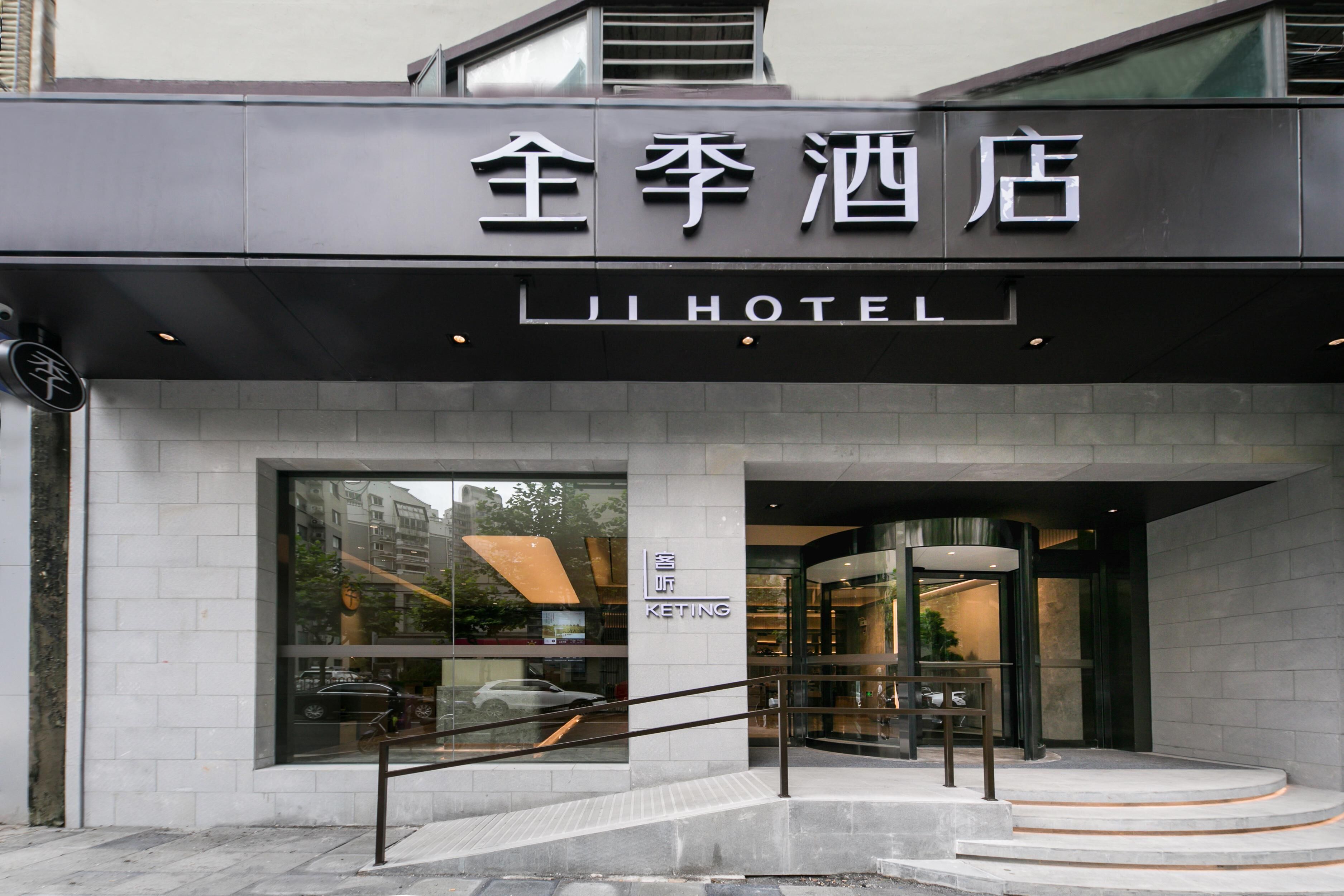 Entrada de hotel com design moderno, destacando uma placa com caracteres chineses e a palavra 'HOTEL' em inglês.