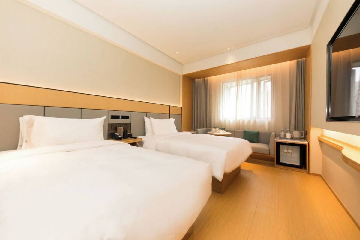 A hotel room with two beds, a TV, a small table, and a window with curtains.