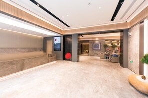 A modern hotel lobby with a reception desk, a digital information screen, a red chair, and a seating area with a plant. - Ji Hotel (Shanghai)