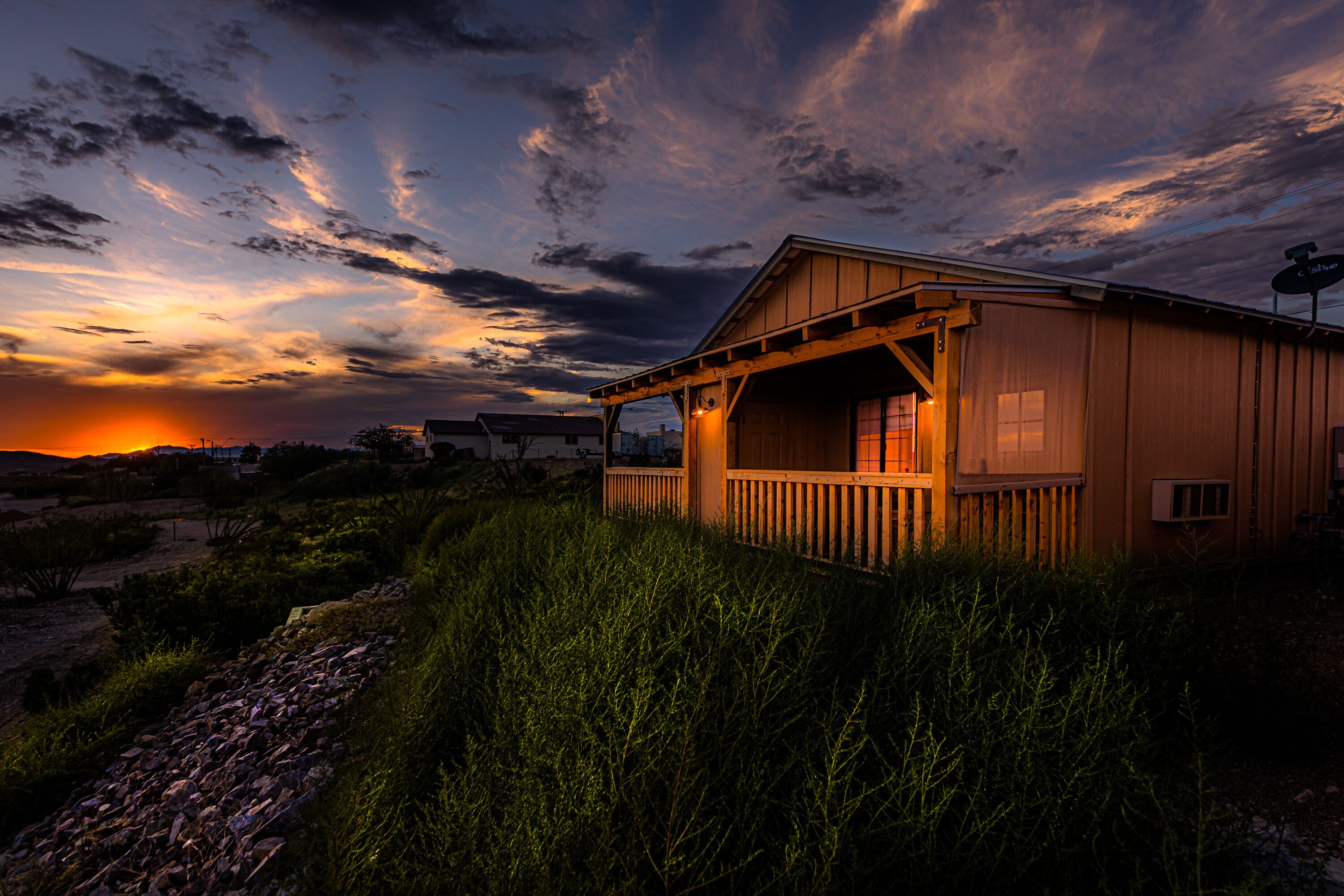 A wooden cabin with a porch, surrounded by tall grass and a rocky path.