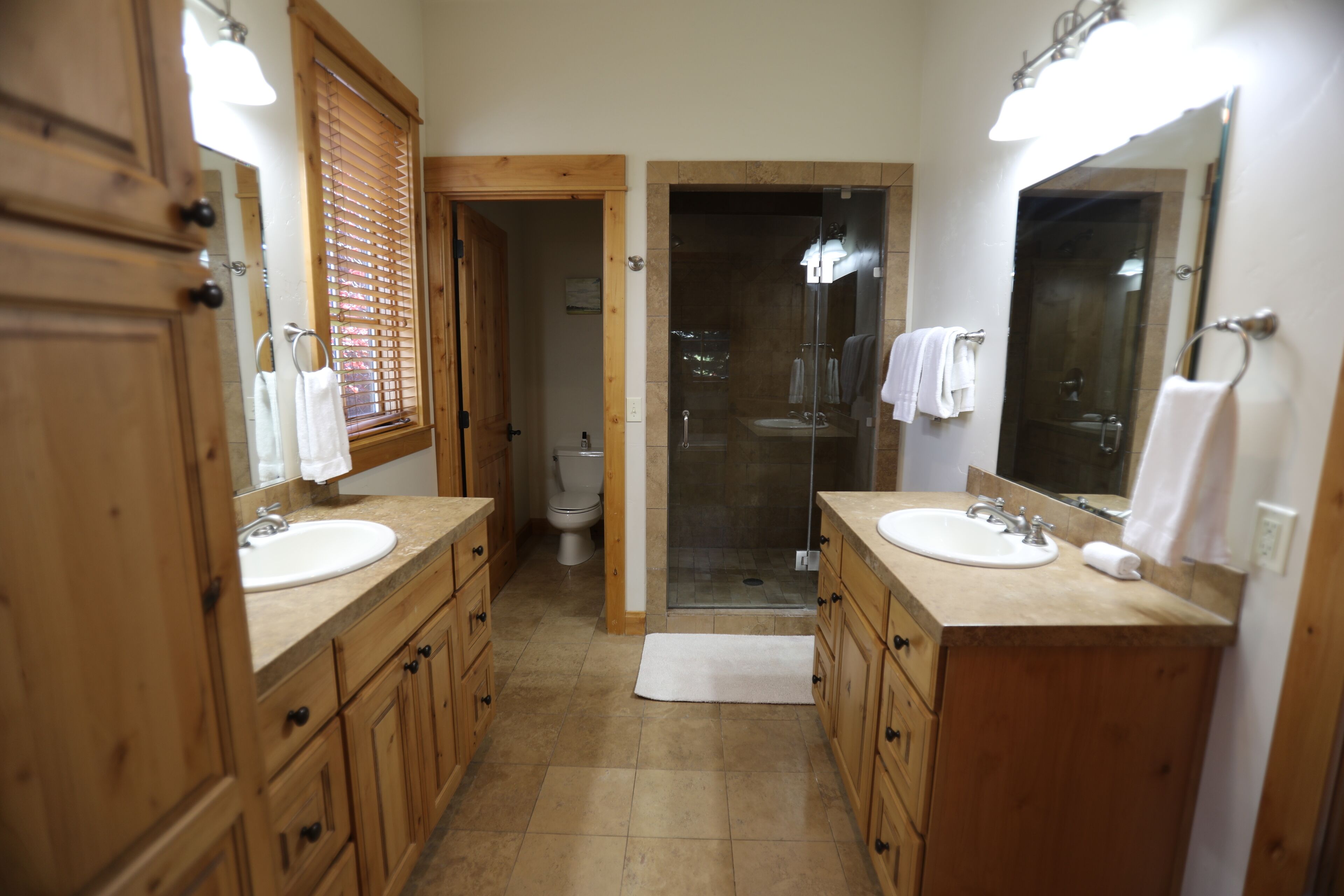 A bathroom with wooden cabinets, two sinks, a shower, and a toilet.
