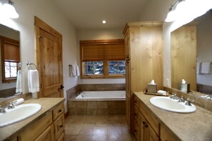 A bathroom with wooden cabinets, a bathtub, two sinks, and a window with a view of trees.