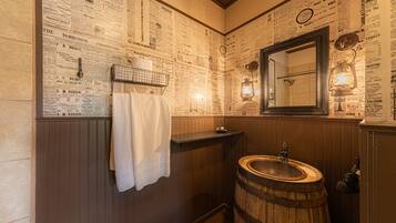 A bathroom with a wooden barrel sink, a towel hanging on a rack, and a mirror with a light fixture.