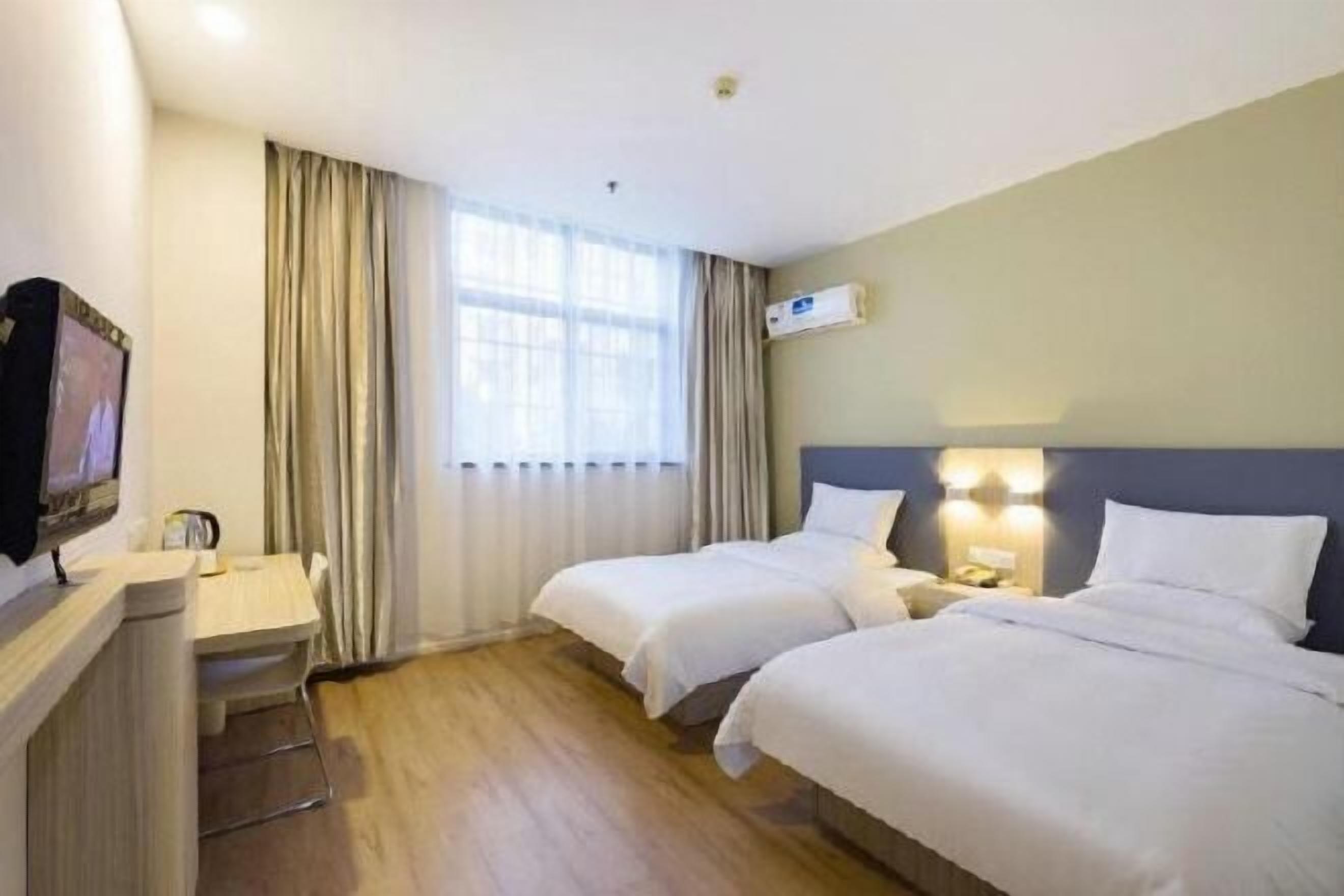 Una habitación de hotel con dos camas, un escritorio, televisión y una ventana con cortinas.