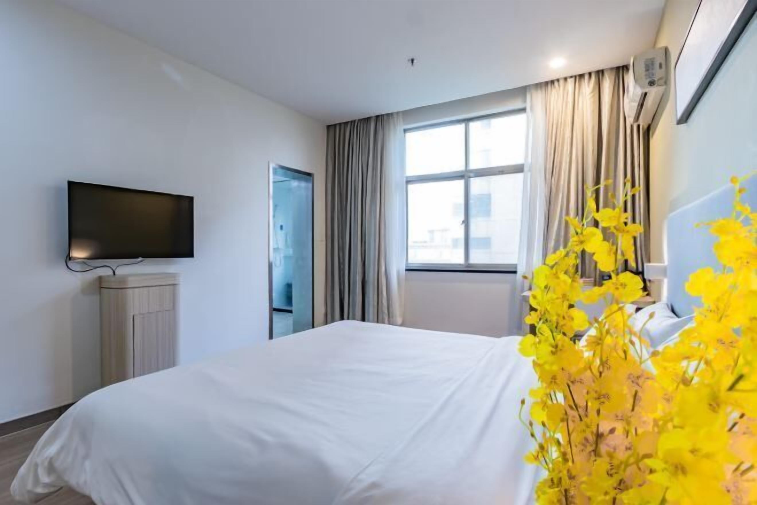 A hotel room with a bed, a flat-screen TV mounted on the wall, a window with curtains, and a radiator.