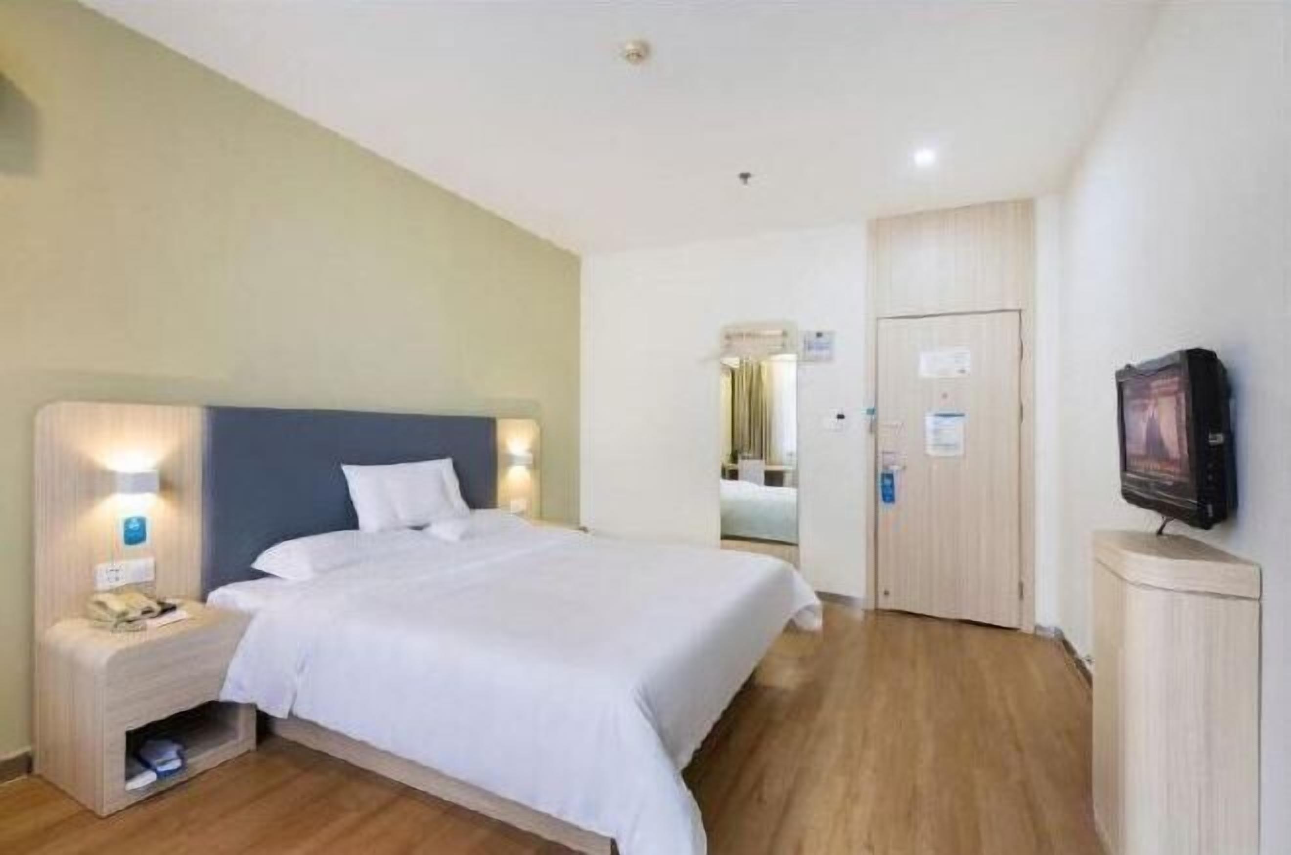 Una camera d'albergo con un letto, lampade ai comodini, una televisione, un armadio e una porta che dà su un'altra stanza.