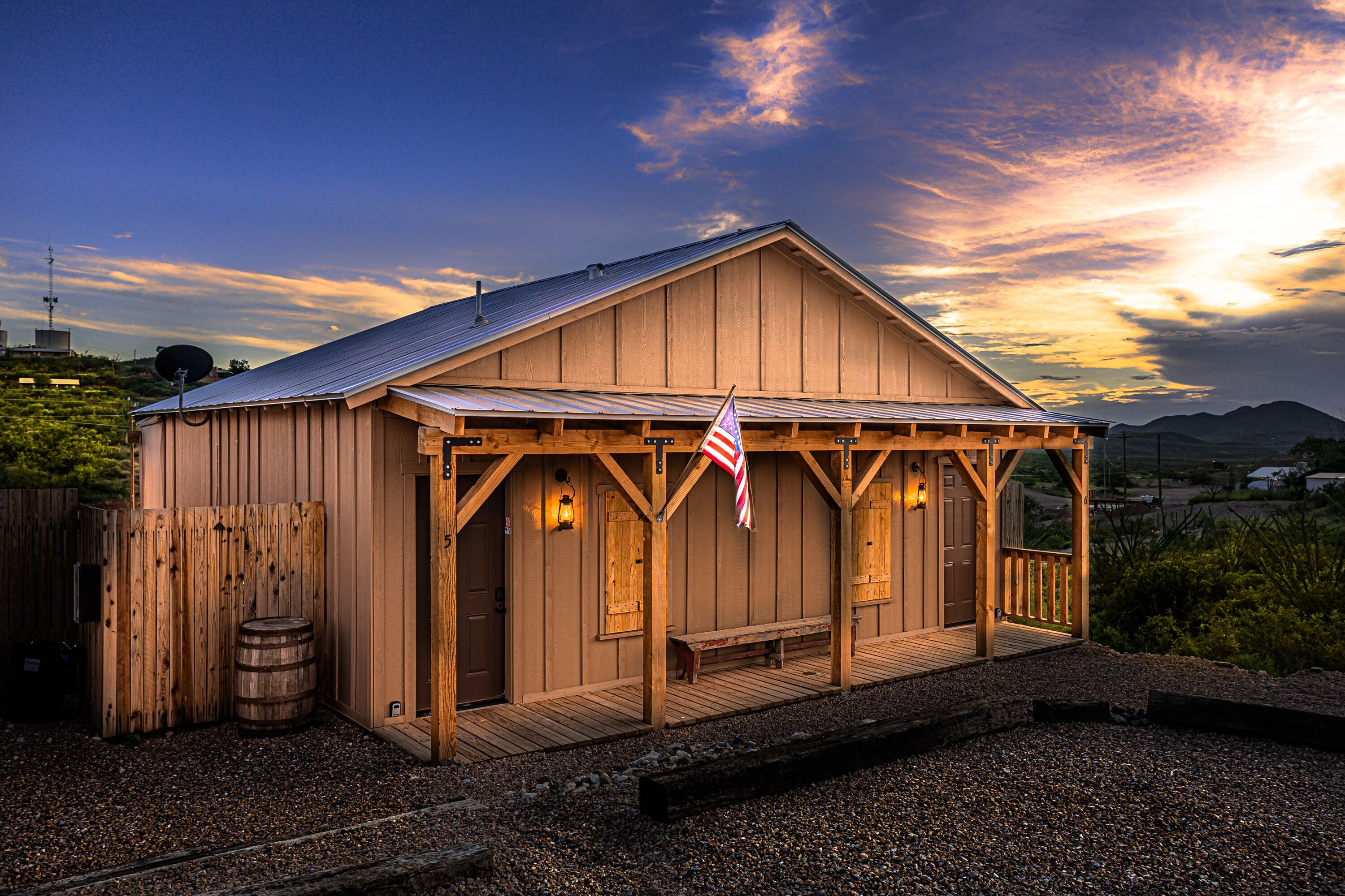 A wooden building with a porch, a flag, and a barrel.