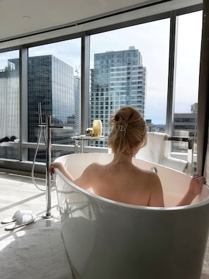 A modern bathroom with a large bathtub, a view of a cityscape through large windows, and a towel rack.