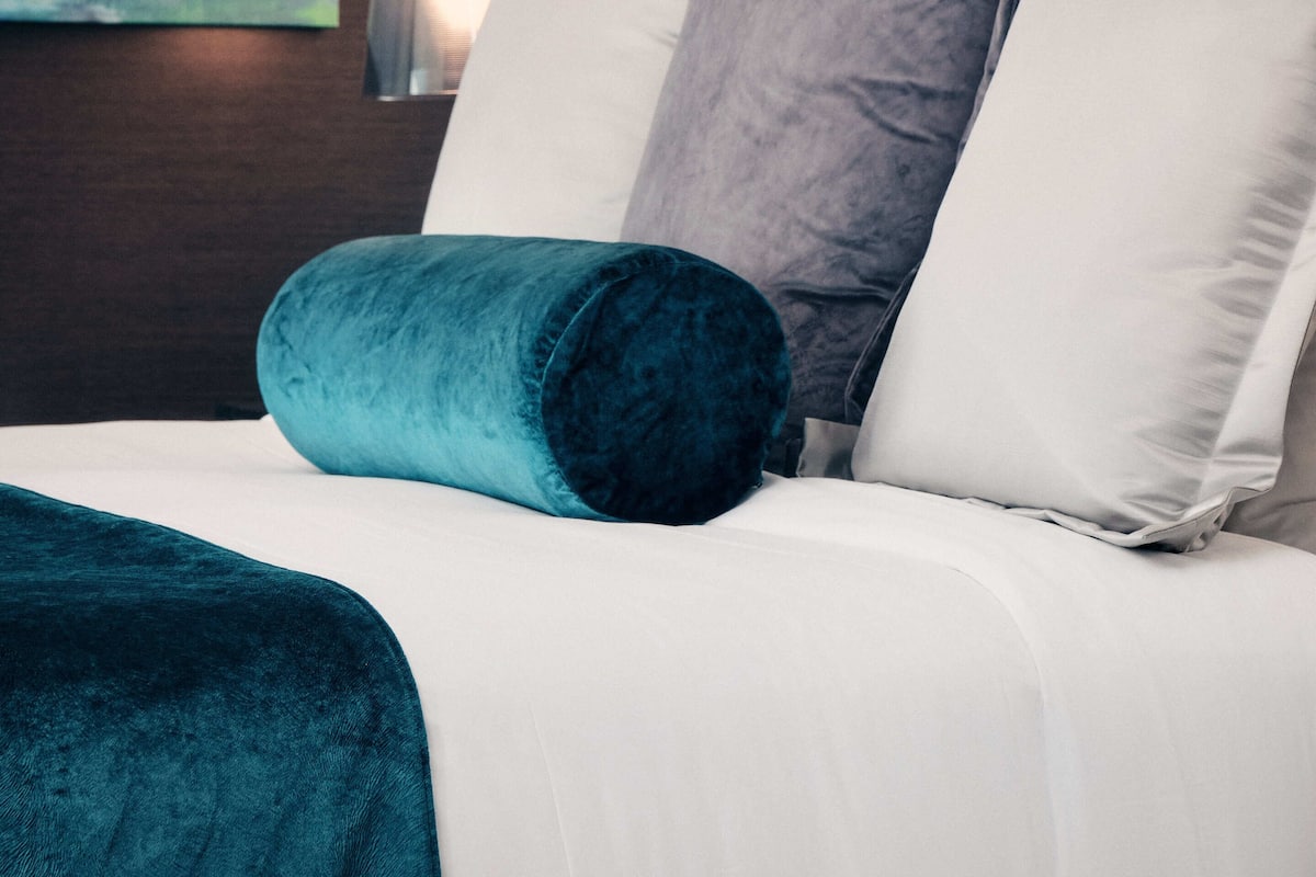 Una cama bien hecha con ropa de cama blanca y aguamarina, una manta color aguamarina oscuro y una almohada.