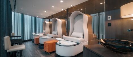 Un moderno salón de spa con tres sillones reclinables, una camilla de masaje y un armario de madera.