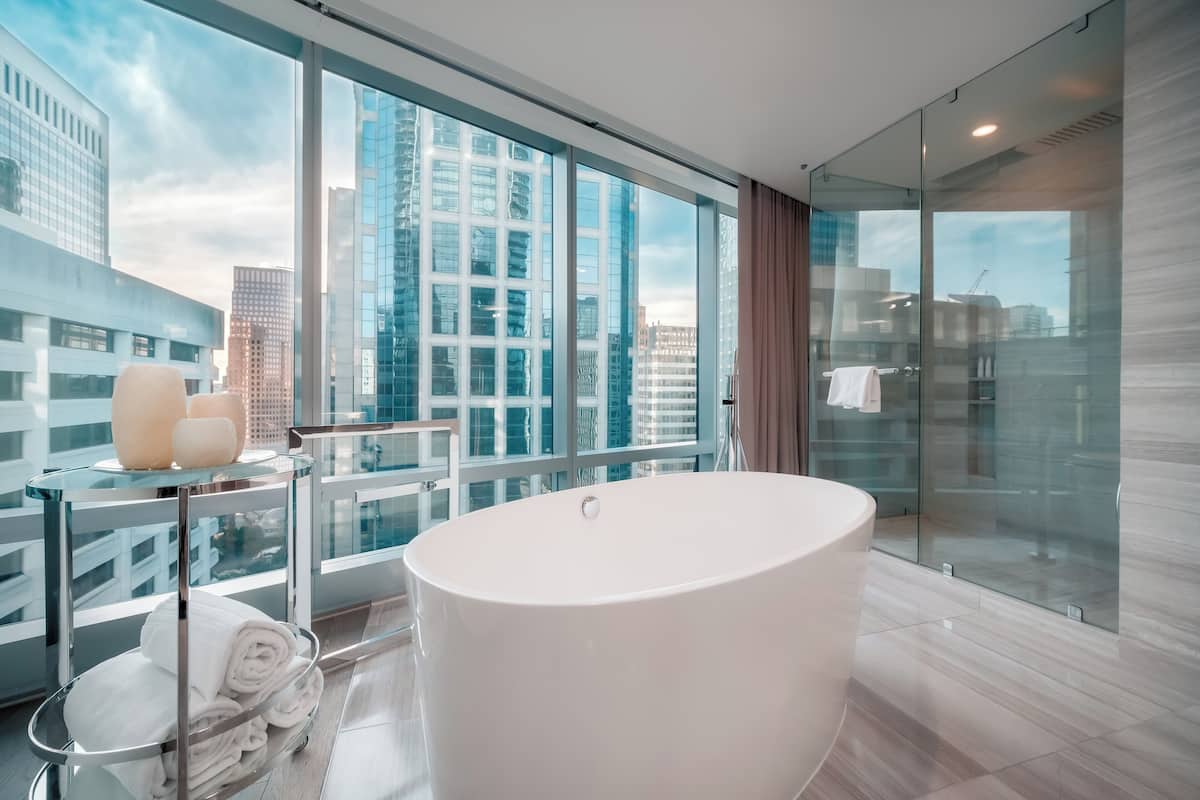 Un baño moderno con una bañera grande, una ducha con cerramiento de vidrio y vistas a edificios de la ciudad.
