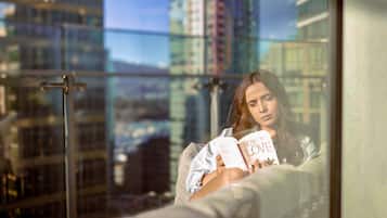 Una persona leyendo un libro titulado "Cómo Amar" en un balcón con vistas a la ciudad.