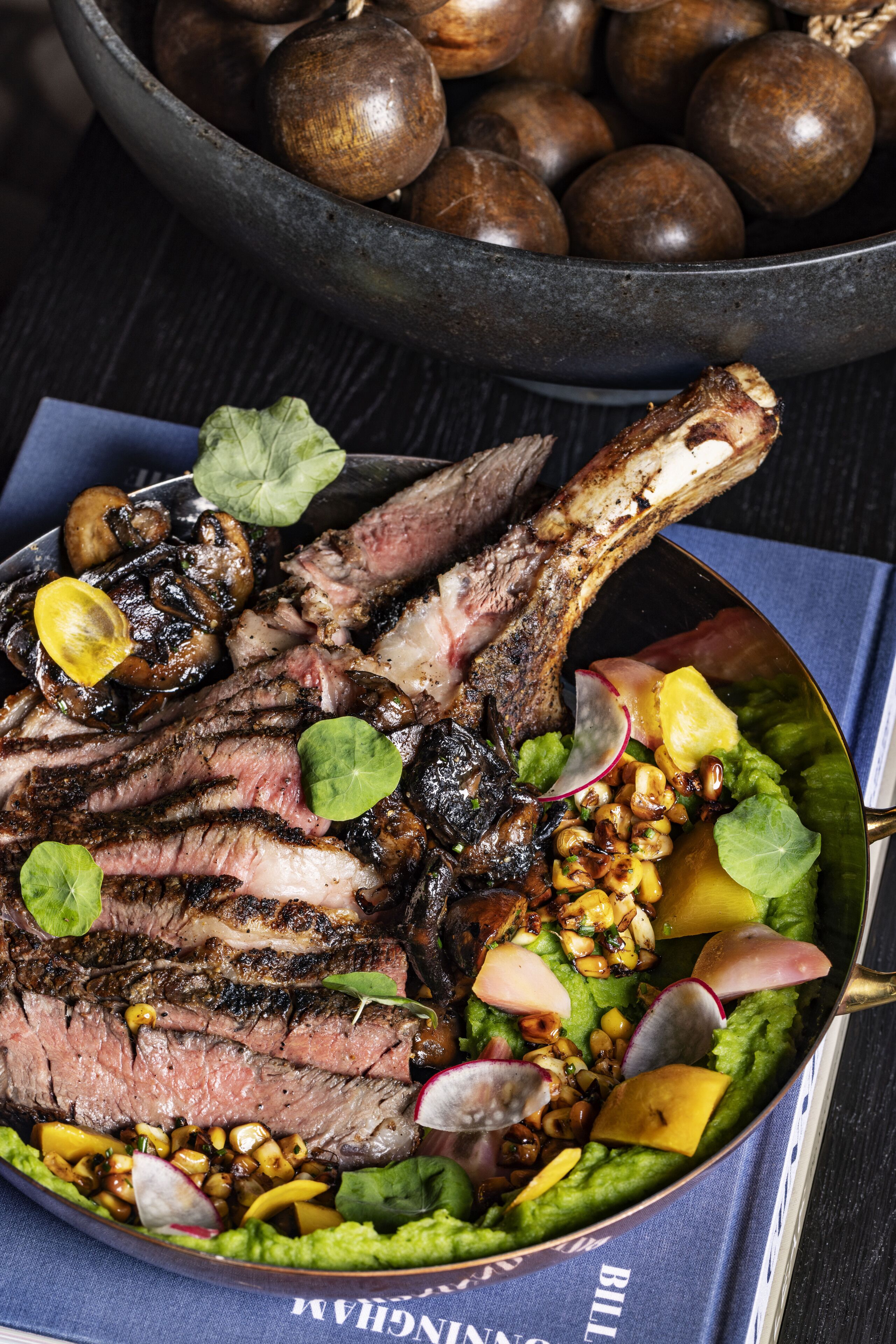 A plate of grilled steak with vegetables and a bowl of mushrooms in the background.
