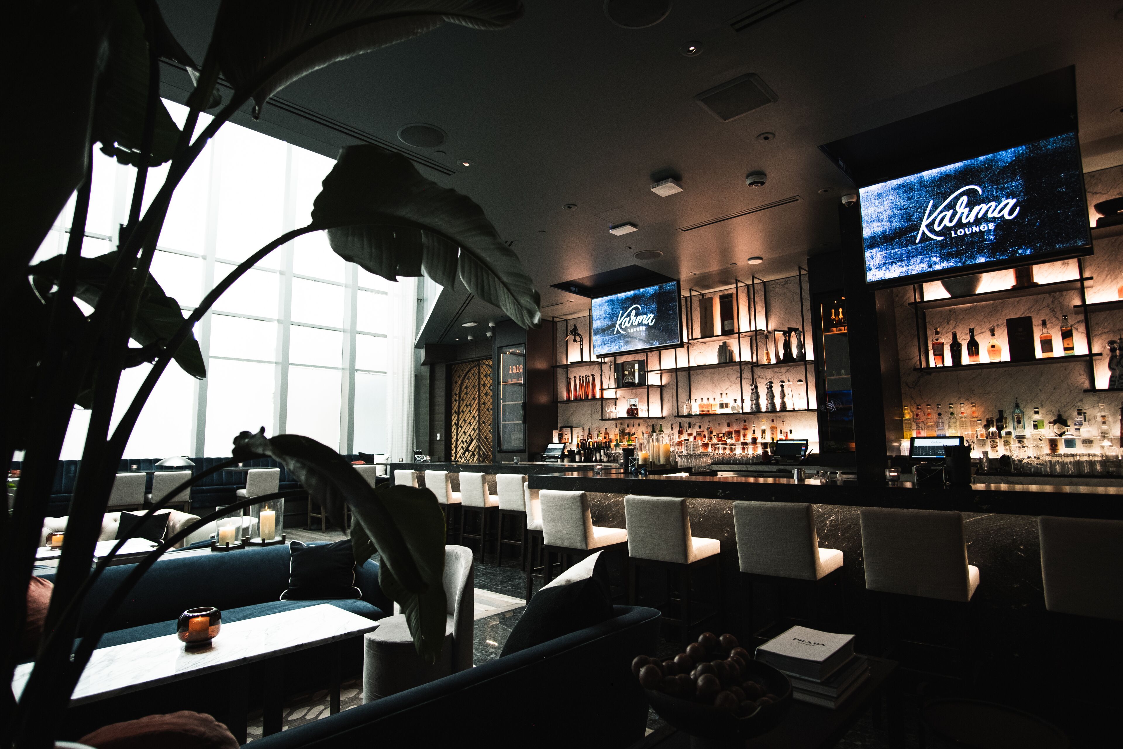 A modern bar area with a large screen displaying "Karma Lounge," bar stools, and a well-stocked bar.