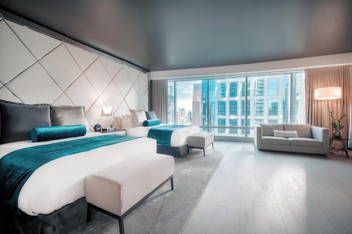 Una habitación de hotel moderna con dos camas, un sofá y un amplio ventanal con vistas a la ciudad.