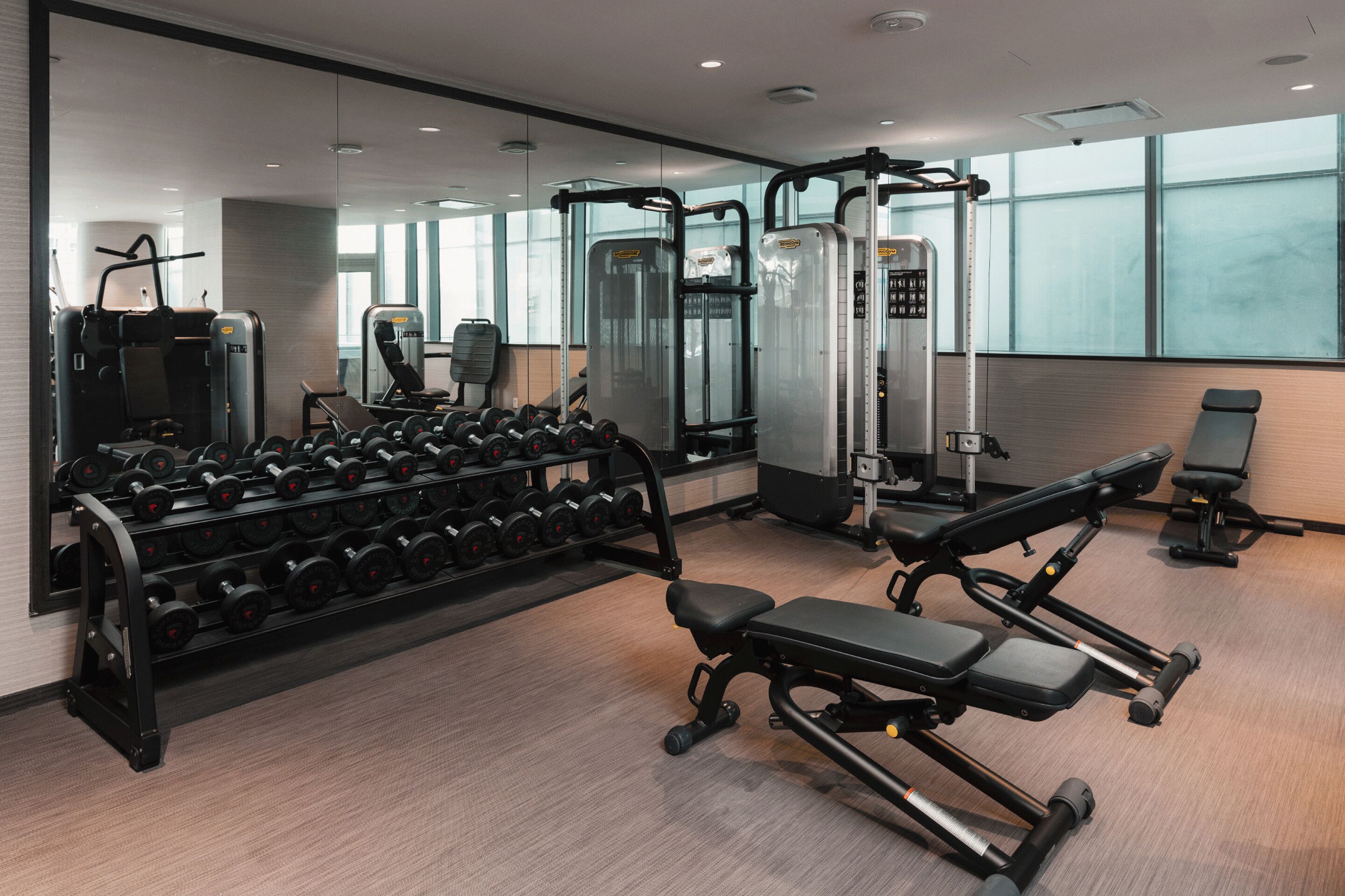 A modern gym with various exercise equipment, including dumbbells, benches, and weight machines.