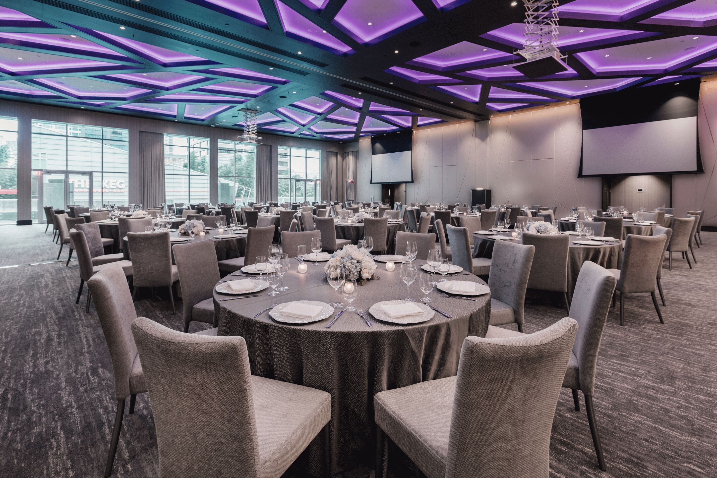 Un salón de conferencias con mesas redondas, sillas y una pantalla grande.