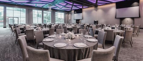 Un salón de conferencias con mesas redondas, sillas y una pantalla grande.