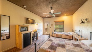 A bedroom with two beds, a desk, a chair, a ceiling fan, and a television on the wall.