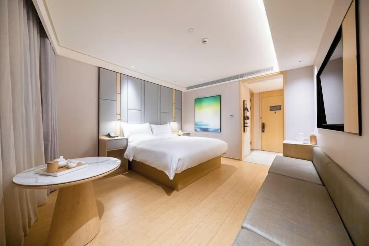 A hotel room with a large bed, bedside tables, a round table, and a view of the hallway.