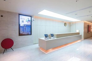 A reception area with a modern design, featuring a reception desk, a digital display, and a red chair. - JI Hotel (Shanghai Dongfang Yidecheng Luheng Road Metro Station) (Shanghai)