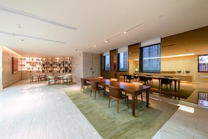 A modern library with a long wooden table and chairs, bookshelves, and a large window. - Ji Hotel (Shanghai)