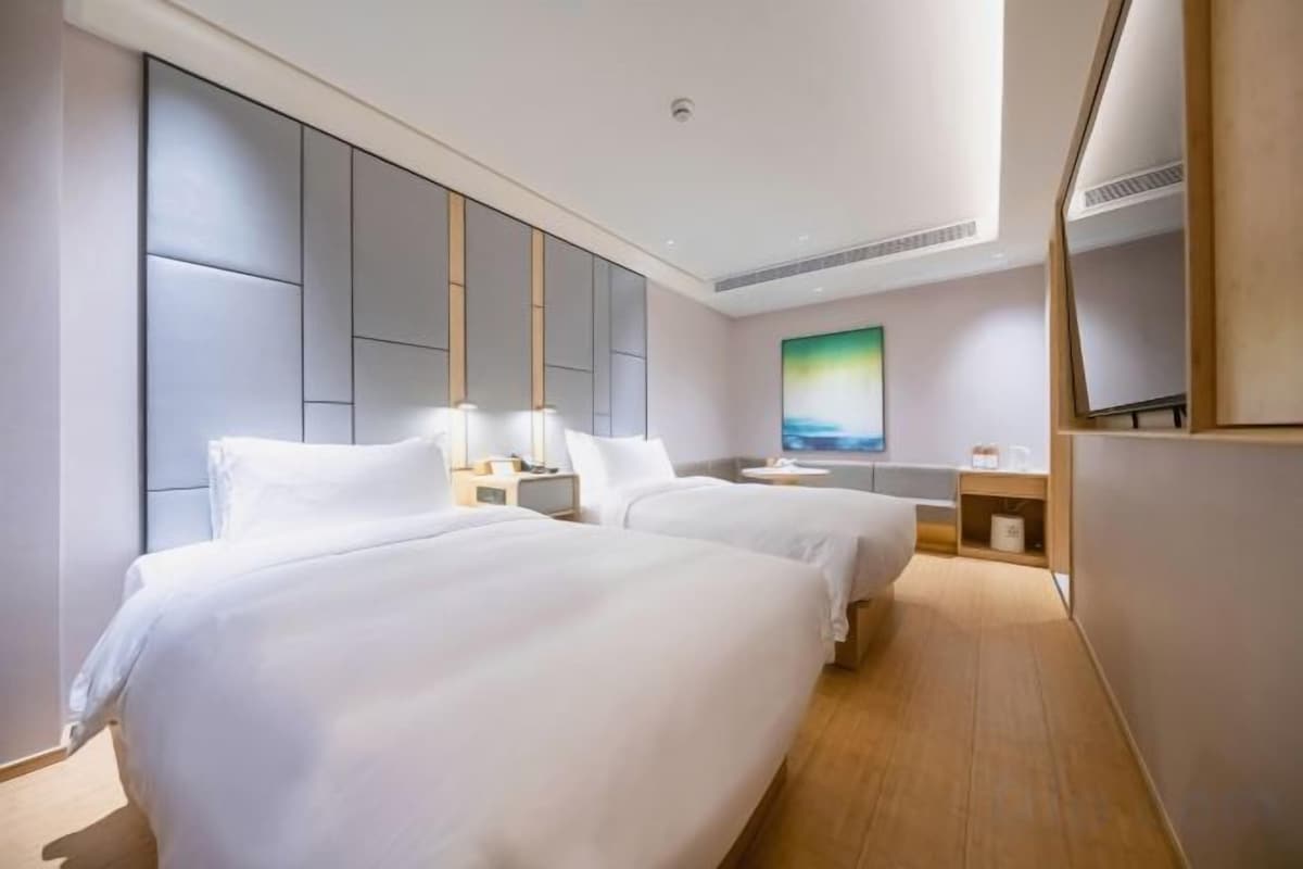 A hotel room with two beds, a large wall-mounted TV, and a painting.