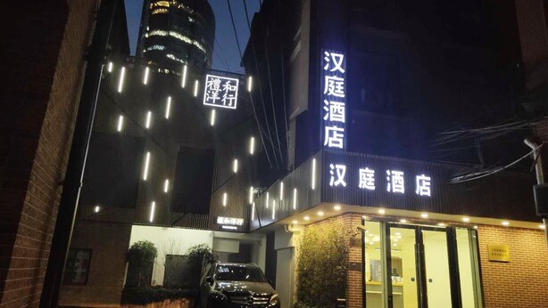 A hotel with illuminated signage in Chinese characters, a parked car, and a building with a visible logo in the background. - Hanting Hotel Shanghai The Bund Jiangxi Middle Roa (Shanghai)