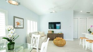 A modern living room with a sofa, a dining table with chairs, a TV mounted on the wall, and a ceiling fan. - New Caribbean home.  Resort access to pool (Islamorada)