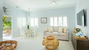 A spacious living room with a light blue wall, a beige sofa, a dining table with chairs, and a television mounted on the wall. - New Caribbean home.  Resort access to pool (Islamorada)