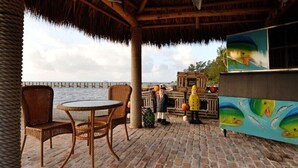 An outdoor seating area with wicker chairs and a round table, a thatched roof, and a view of the sea. - Luxurious Caribbean 2 Bedroom 2 Bath Home (Islamorada)