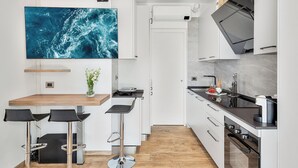 Et moderne køkken med hvide skabe, et stort fladskærms-tv monteret over disken, og et træspisebord med barstole.