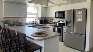 A modern kitchen with white cabinets, a stainless steel refrigerator, a microwave, and a gas stove. There is a large island with a coffee maker and a kettle. - Sandy Feet Retreat - 3Bdrms, Pool, Steps to Beach (Fort Myers Beach)