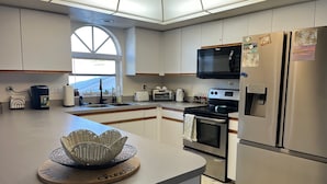 A modern kitchen with a central island, stainless steel appliances, and a large window providing natural light. - Sandy Feet Retreat - 3Bdrms, Pool, Steps to Beach (Fort Myers Beach)
