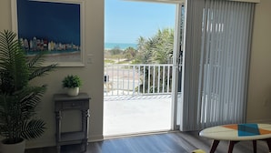 A room with a large window, a potted plant, a painting, and a table. - Sandy Feet Retreat - 3Bdrms, Pool, Steps to Beach (Fort Myers Beach)